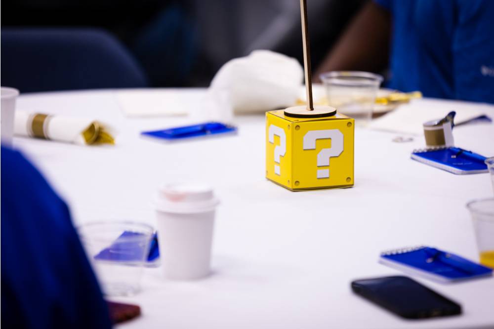 Table displays: blue pads of paper with pens, a yellow Mario themed question block, and a table number stand